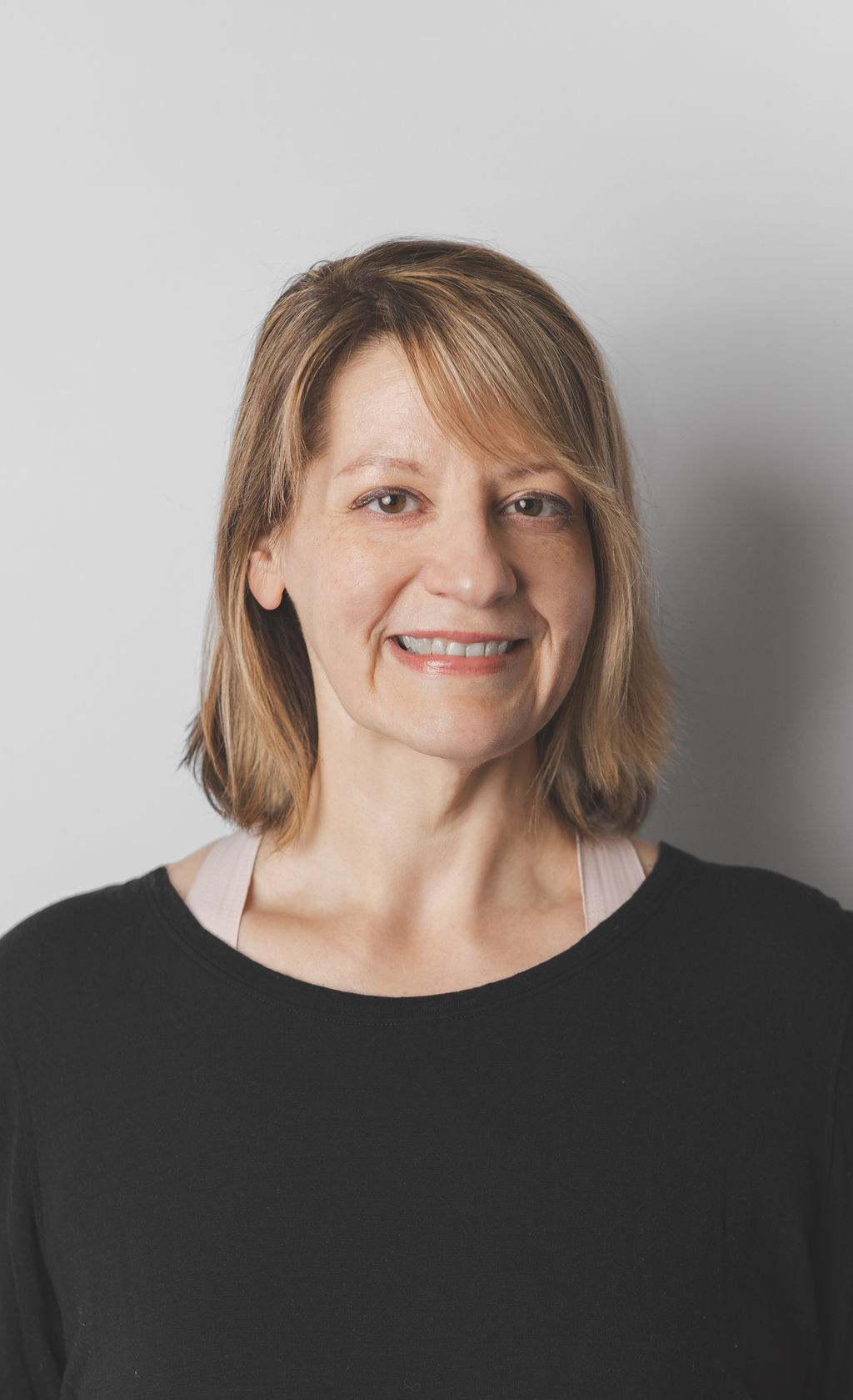 Smiling Be Fitness instructor wearing black top against neutral background